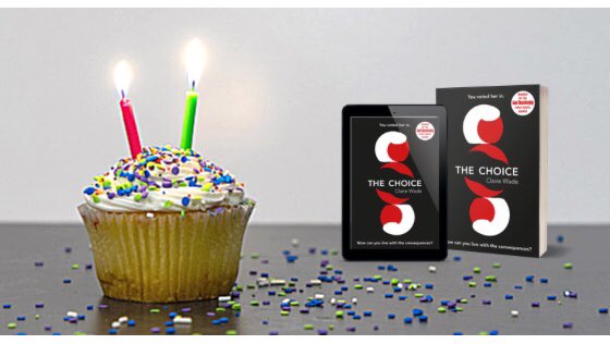 A cupcake with two lit candles beside two copies of The Choice one on an e-reader the other paperback.